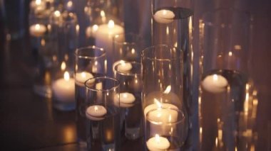 Floating candles burning in glass vases filled with water near a white wedding table tablecloth. Boho rustic decor. Birthday party decoration. Sorrow, funeral or mourning candles concept.
