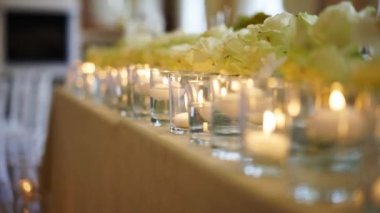 Wedding rustic style decor with dishes, drinks and roses in white and blue colours on table setting at restaurant. Banquet hall interior floristic details, flowers in glass vases filled with water.