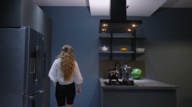 Young woman takes a chocolate pie out of the oven. Girl makes pastry at home. Female performs homemade baking in a stylish modern kitchen. Housewife preparing food on a cooking island. Smelling food.