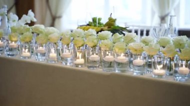 Wedding rustic style decor with dishes, drinks and roses in white and blue colours on table setting at restaurant. Banquet hall interior floristic details, flowers in glass vases filled with water.