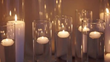 Floating candles burning in glass vases filled with water near a white wedding table tablecloth. Boho rustic decor. Birthday party decoration. Sorrow, funeral or mourning candles concept.