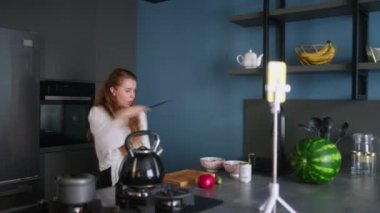 Food blogger woman cooking fresh vegan salad of vegetables in kitchen studio and filming funny dancing for social media content on a smartphone for a video channel. Female influencer streaming.