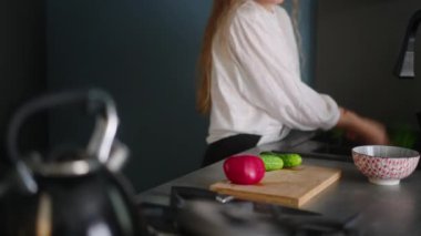 Beyaz kadın sebze yıkıyor ve salata yapmaya başlıyor. Genç dişi sebzeleri yıkar ve salata pişirir. Kız salatalık ve domatesleri doğrama tahtasında kesiyor. Kadın modern mutfakta yemek pişiriyor.
