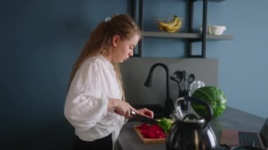Stressed woman in hurry on multitasking rush on remote job at home. Distracted female cooking salad, answer calls, chatting with clients, works on laptop simultaneously at kitchen. Freelancer girl.