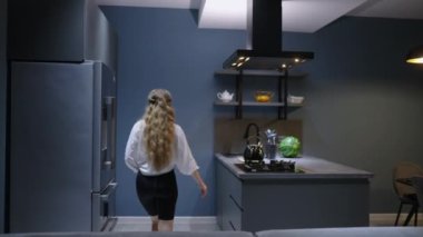 Young woman takes chocolate pie out of the oven. Girl makes pastry at home. Female performs homemade baking in stylish modern kitchen. Housewife prepares and smells food on kitchen island, takes knife