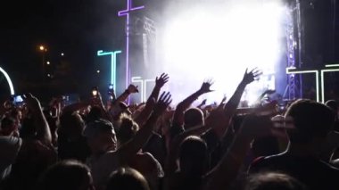 2019-08-09 - Mariupol, Ukraine. MFest festival. People silhouettes waving hands, taking photos or recording videos of live music concert with smartphones at an open air fest. Colorful stage lighting.