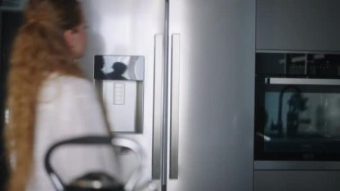 Buzdolabından sebze alan genç bir kadın. Buzdolabından domates alan kız. Kadın atıştırmalık sağlıklı bir şeyler yiyor. Güzel beyaz kadın buzdolabını açıp kapıyor.