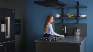 Pretty young caucasian woman wearing headband wipes surfaces at home in a modern stylish kitchen, keeping house neat. Housewife cleaning kitchen surface with rag. Young female doing household chores