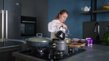 Kadın kahve ve kibrit çay yapıyor, modern mutfak adasında tavadan lezzetli yemekler tadıyor. Genç bayan aşçılar yemek yer. Kız bardaklara kaynamış su doldurup omlet yiyor..