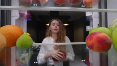 View from inside the fridge - woman opens side by side fridge doors, puts tomatos, then closes it. Female puts vegetables into refrigerator. Pretty girl on healthy diet.