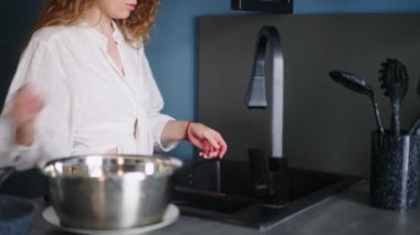 Young caucasian woman washes pots under running water in sink in modern kitchen. Housewife is rinsing the pan on a kitchen island. Female performing the washing-up in high-tech kitchen