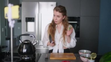Yemek blogcusu kadın mutfak stüdyosunda taze sebze salatası pişiriyor video kanalı için akıllı telefondan ders veriyor. Kadın nüfuz eden kişi yeşillikleri keser. Yeşiller sağlıklı bir diyetten bahseder..