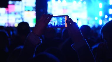 2019-08-09 - Mariupol, Ukrayna. MFest festivali. Erkek eli siluetinin fotoğraf çekimini kapat, açık hava festivalinde akıllı telefonlu canlı müzik konserinin videosunu çek. Parlak renkli sahne ışığı.