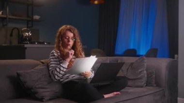 Gözlüklü kız ders çalışıyor, evde dizüstü bilgisayarla ödev yapıyor geceleri oturma odasında kanepede oturuyor. Odaklanmış kadın serbest yazar. Klavye üzerine yazı yazıyor. Proje üzerinde çalışıyor..