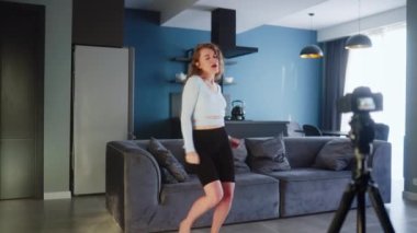 Sosyal medya platformunda beğeniler ve takipçiler için moda dans yarışması videosu kaydeden güzel bir kız. Komik dans eden bir kadın, ev stüdyosundaki oturma odasında gösterisini kameraya çekiyor..