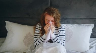 Üşütmüş, öksüren ve burnunu sümküren boğazı, ateşi ve baş ağrısı olan bir kadın. Genç beyaz kadın koronavirüsten muzdarip. Covid19. İzolasyon alnına dokunurken.