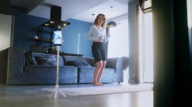 Sosyal medya platformunda beğeniler ve takipçiler için moda dans yarışmasının videosunu kaydeden hoş bir kız. Komik dans eden bir kadın, bir stüdyoda akıllı telefon kamerasıyla kendi performansını filme alıyor..