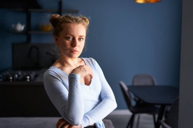 Photo of healthy lovely young caucasian calm woman with natural makeup holding green apple over dark stylish modern kitchen background. Girl with resting face standing with green fresh fruit at home.