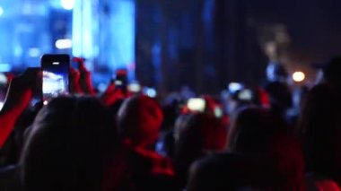 Close up of man hands silhouette taking photo or recording video of live music concert with smartphone at open air festival. Bright colorful stage lighting. Fans at the favourite band performance.
