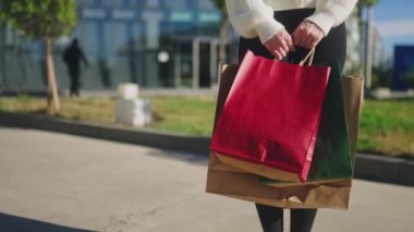 Şehirde alışveriş merkezinin yanında elinde kağıt torbalarla duran kadına yakın durun. Kara Cuma satışından mal alan bir kızın düşük açılı görüntüsü. Ağır çekim. Sağ iz sürme çekimi, kopyalama alanı.