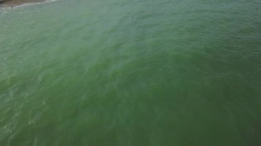 Sahildeki saman şemsiyelerin havadan görünüşü. Okyanus dalgaları kumlu kıyıları yıkıyor. Lüks bir tropikal tatil köyünün sakin sahil şeridi..