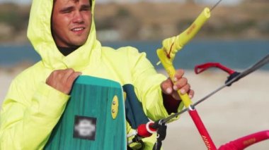 Islak uçurtma sörfçüsü sahil kenarında uçurtma çubuğuyla bekliyor. Freestyle Kiter, uçurtma sörfü antrenmanından sonra gölde kameraya bakıyor. Aşırı su sporları. Yavaş çekim 120 fps görüntü.