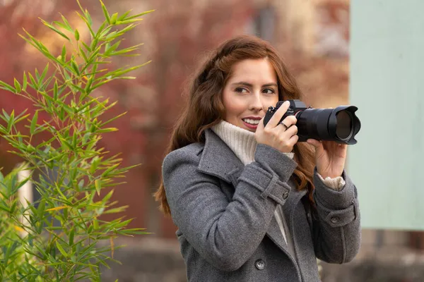 Jonge vrouw kijkt rond met haar fotocamera en glimlacht in een park — Stockfoto