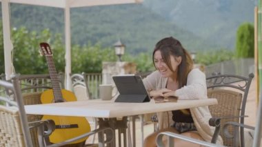 Terasta oturan tabletli bir kadın video görüşmesinde konuşuyor. 