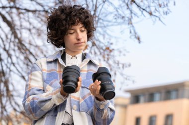 Kıvırcık saçlı genç esmer kadın fotoğraf makinesi için lens seçiyor.