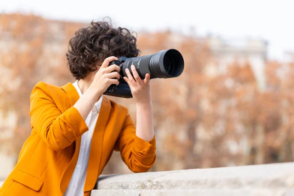 Young brunette woman with curly hair taking a picture with telephoto lens — Stock Photo, Image