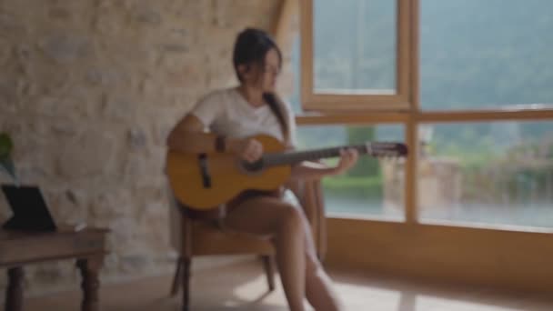 Жінка грає на іспанській гітарі біля вікна у великій кімнаті. — стокове відео