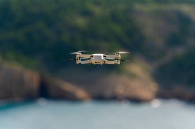 Küçük dron hala dağlarda ve deniz arka planında uçuyor.