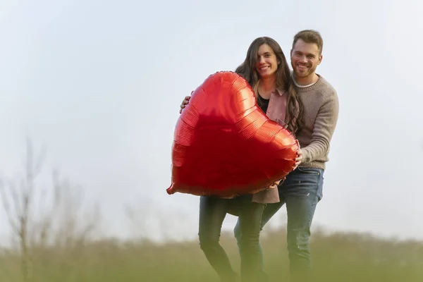 Młoda para świętuje walentynki trzymając czerwony balon w kształcie serca — Zdjęcie stockowe