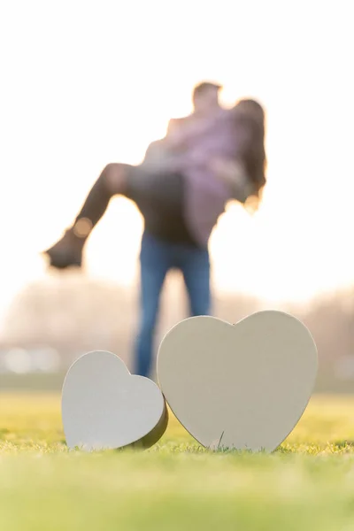 Młoda para przytulająca się za dwoma kształtami serca w parku w Walentynki — Zdjęcie stockowe