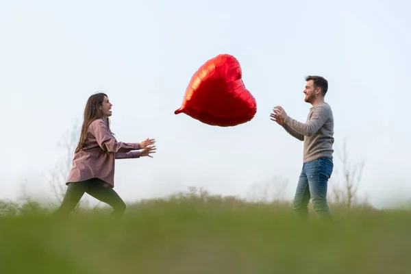 Młoda para świętująca walentynki bawiąca się balonem w kształcie serca — Zdjęcie stockowe