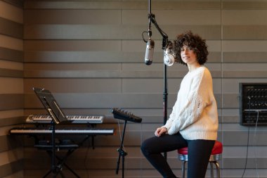 Genç kıvırcık saçlı bir kadın gerçek bir stüdyoda şarkı söylüyor..