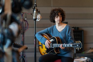 Genç bir şarkıcı kadın gitarıyla berbat bir stüdyoda şarkı kaydediyor.