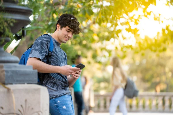 Genç bir öğrenci telefonuna bakıyor ve sokakta gülümsüyor.