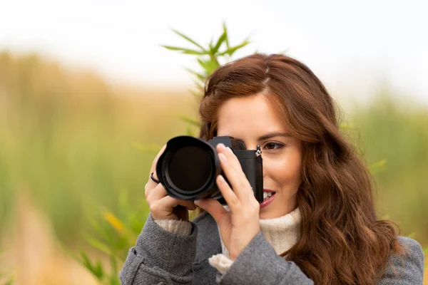 红头发的年轻女子带着相机在外面拍照 — 图库照片