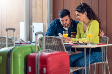 Telefona bakan ve otel restoranında kahvaltı yapan turist çifti.