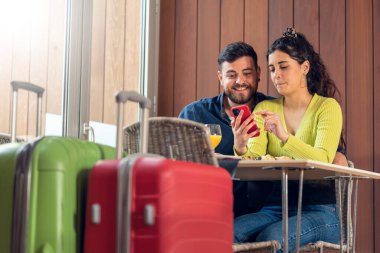 Telefona bakan ve otel restoranında kahvaltı yapan turist çifti.