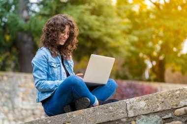 Parkta gülümseyen ve bilgisayarını kullanan genç bir kadın.