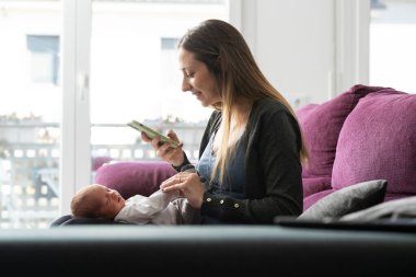 Genç anne kanepede yeni doğmuş bebeğine fotoğraf çekiyor.