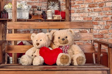 İki oyuncak ayı yan yana bir bankta oturuyor, birbirine sokulmuş, yumuşak bir oyuncaktan yapılmış bir kalple, önden bakıldığında