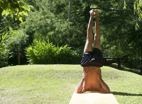 An adult man doing yoga on the grass outdoor, in a relax position