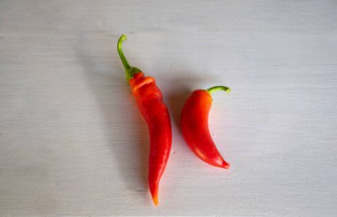 Two fresh red chilli peppers on a white wood background