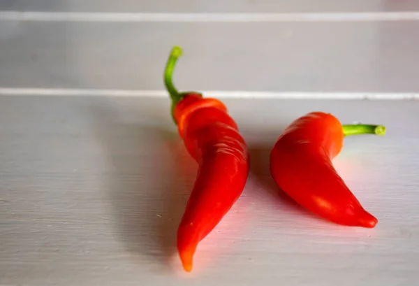 Two red chilli peppers on a white wood background