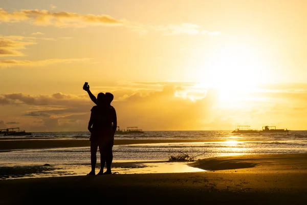 A couple in the beach taking a selfie with the sunset in the valentine day