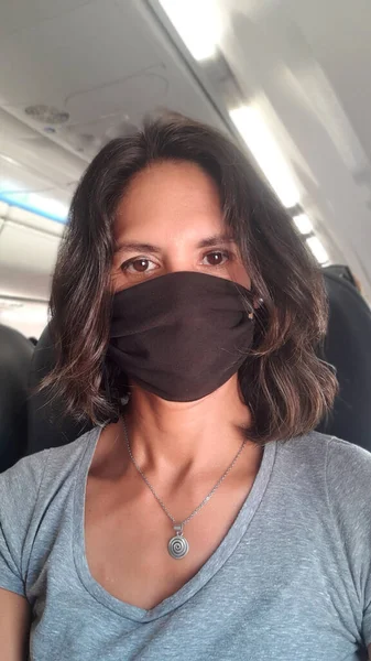 Woman with protective mask taking a selfie in the cabin of airplane