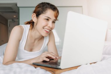 Yatakta dizüstü bilgisayarla çalışan bir kadın. Otelden çalışma kavramı.